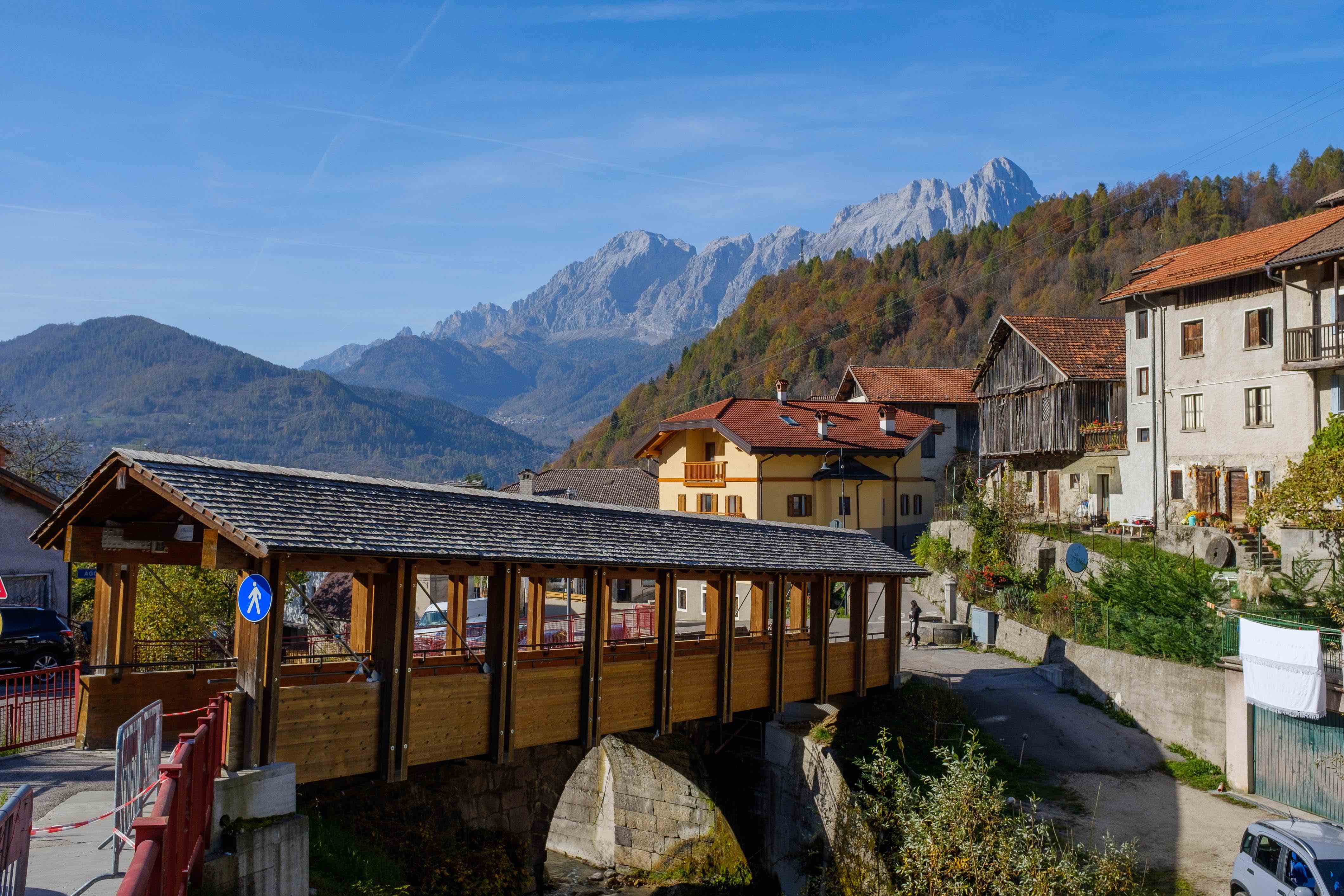 photo of an Italian alpine village along a river with tall mountain peaks behind