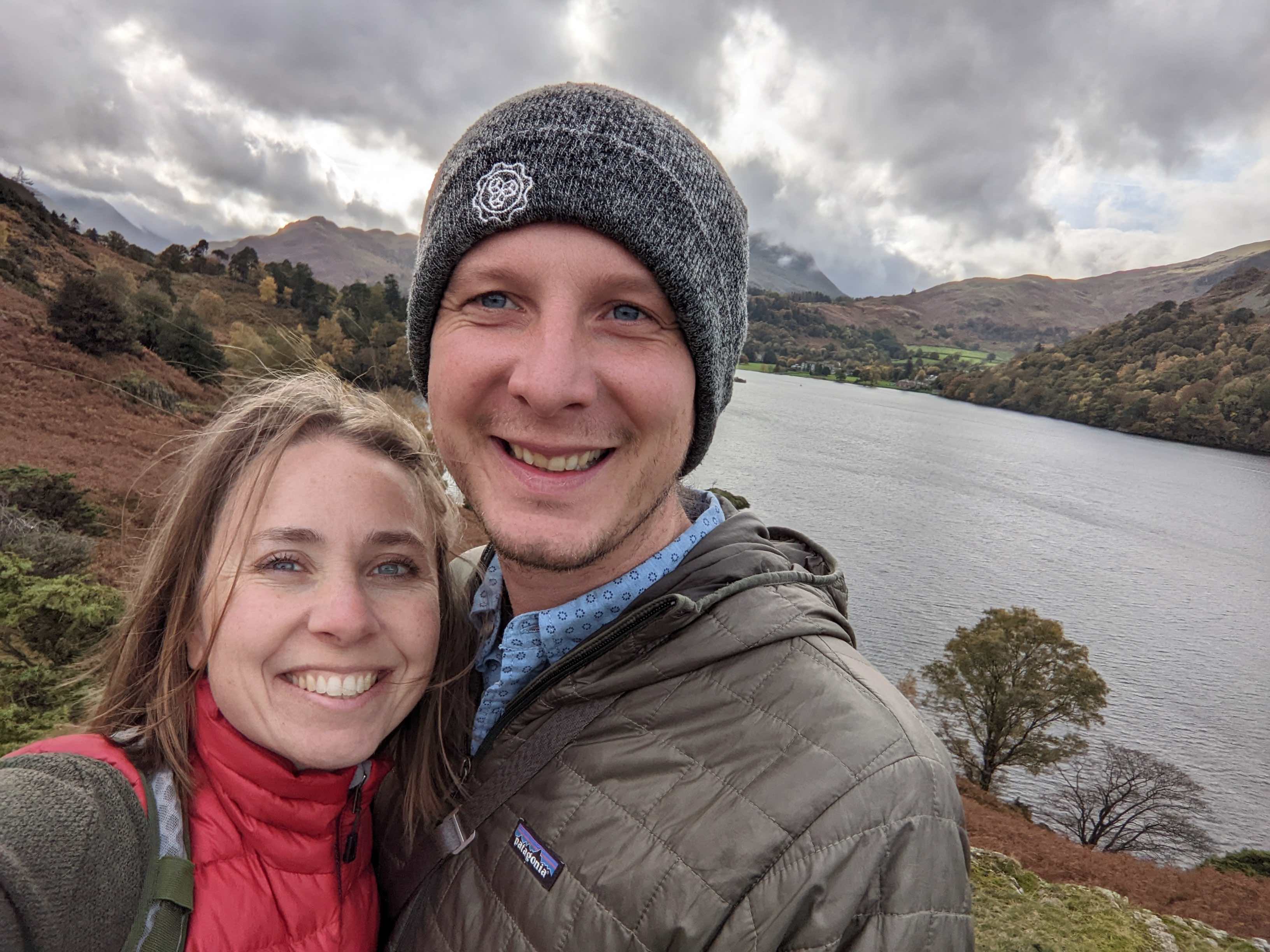 a selfie of a white man and woman smiling with a lake behind them